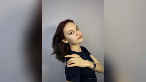Young woman with long brown hair wearing a navy blue t-shirt posing against a plain grey background.