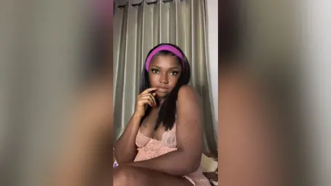 Young woman in a pink lace camisole and purple headband posing indoors with a soft, serene mood.