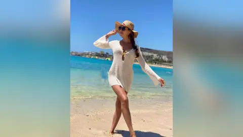 Stylish woman in a white knit mini dress and sun hat enjoying a sunny summer day at a tropical beach.