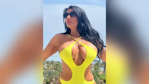 MissyJolie poses outdoors in a bright yellow cut-out bodysuit with a deep plunging neckline and long black hair.