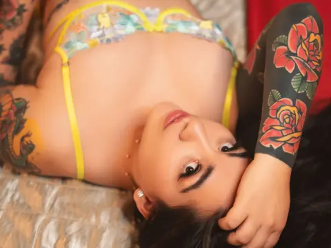 Tattooed woman in yellow lace lingerie lying on a bed with a relaxed, intimate mood.