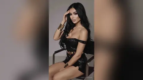 Glamorous woman in a black leather outfit and gold cuffs posing confidently in a studio setting.