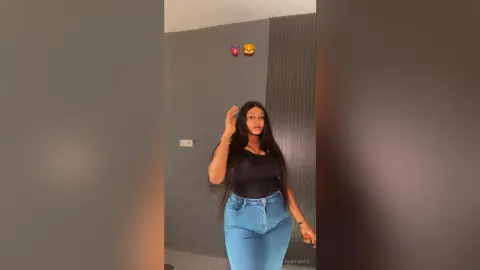 Young woman in a black bodysuit and blue jeans posing in a modern minimalist room.