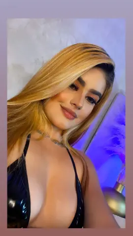 Smiling blonde woman in a black halter top posing in a room with purple ambient lighting.