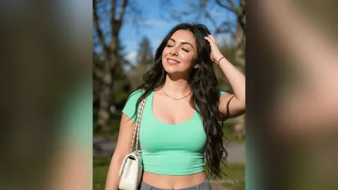 Smiling woman in a mint green tank top enjoying a sunny day in a lush green park.