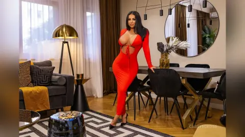 Elegant woman in a tight red evening dress posing in a modern luxury living room with gold decor.