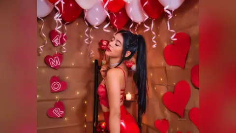 JessieLiu poses in red lace lingerie and a red skirt, looking over her shoulder against a backdrop of red and white balloons and heart decorations.