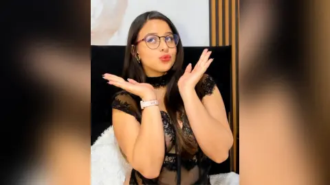 Young woman with glasses in a black lace top smiling playfully in a modern indoor setting.