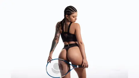 Athletic woman with braided hair in black sports bra and briefs holding a tennis racket against a white background.