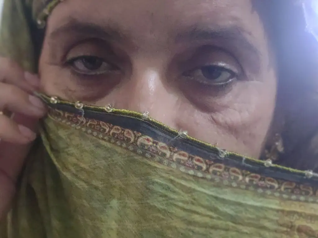 Close-up portrait of a woman with dark eyes partially covered by a patterned green traditional dupatta scarf.