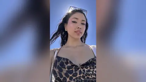 Smiling woman in leopard print top and sunglasses enjoying a sunny day outdoors.