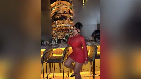 Elegant woman in a red lace cocktail dress standing in a luxury bar with a glowing liquor shelf background.