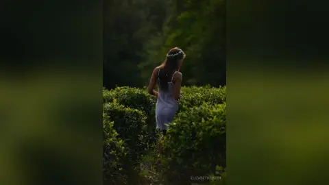Dreamy woman in a white lace dress walking through a lush green garden at twilight.
