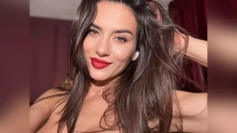 Smiling brunette woman with long wavy hair and bold red lipstick in a warm indoor setting.