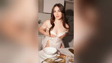 KeiraHarts wears a white lace teddy, pulling down the neckline to show her cleavage while sitting at a table with white bowls.