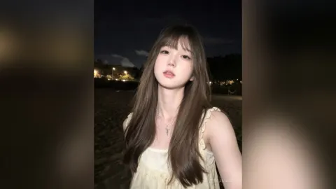 TessaMabel — TessaMabel poses outdoors at night wearing a white lace sleeveless top with long brown hair.