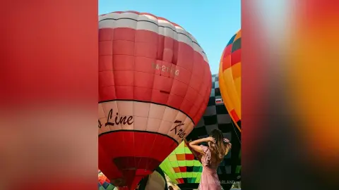 StacyHarland stands before a large red and white hot air balloon, running her hands through her long brown hair.