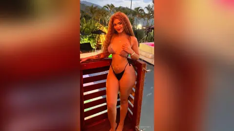 Smiling woman in a brown bikini posing on a tropical resort balcony at sunset.