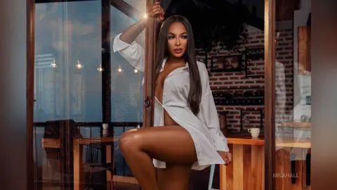 Elegant woman in a white button-down shirt posing by a window in a modern urban apartment at sunset.