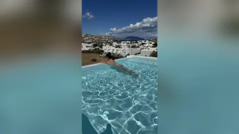Relaxed woman in a bikini swimming in a luxury infinity pool overlooking a Mediterranean coastal village.