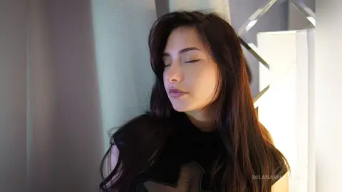 Serene young woman with long dark hair in a black outfit relaxing in soft, warm indoor lighting.