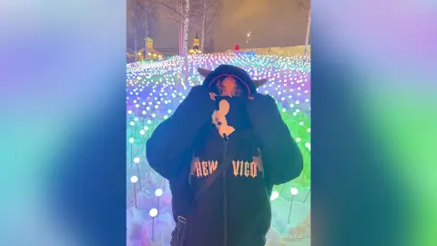 Person in a black hoodie standing in a dreamy field of glowing purple and blue lights at night.