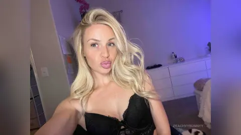 Blonde woman in black lace lingerie making a playful expression in a room with blue mood lighting.