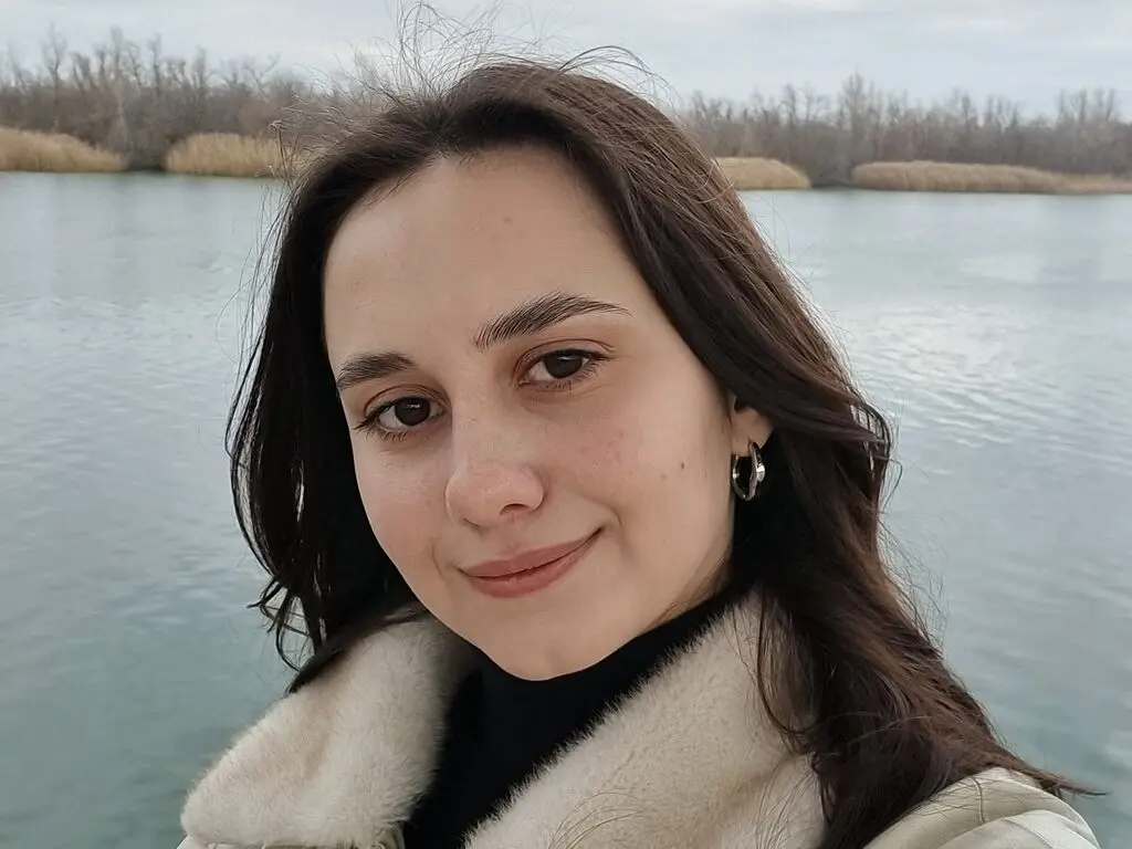 LateshaKaspar smiles for a selfie outdoors by a lake, wearing a white fuzzy coat and black top.