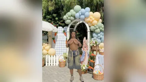 Woman in grey cargo shorts standing by an Easter celebration balloon arch and bunny decor outdoors.