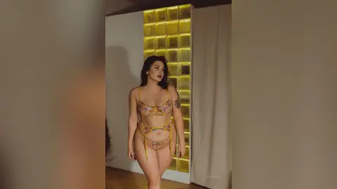 Woman in floral print bikini standing in a modern room with warm lighting and glass block wall.