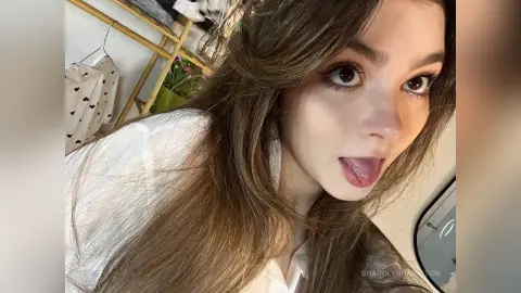 Young woman with long brown hair wearing a white shirt in a bright indoor setting with a soft, natural mood.