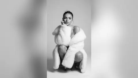 Elegant woman in a white faux fur wrap posing against a minimalist studio background in a black and white portrait.