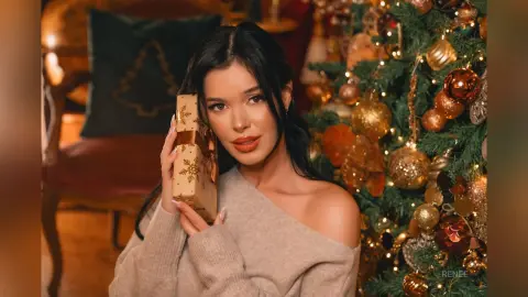Young woman in a beige sweater holding a wrapped gift next to a decorated Christmas tree in a cozy setting.