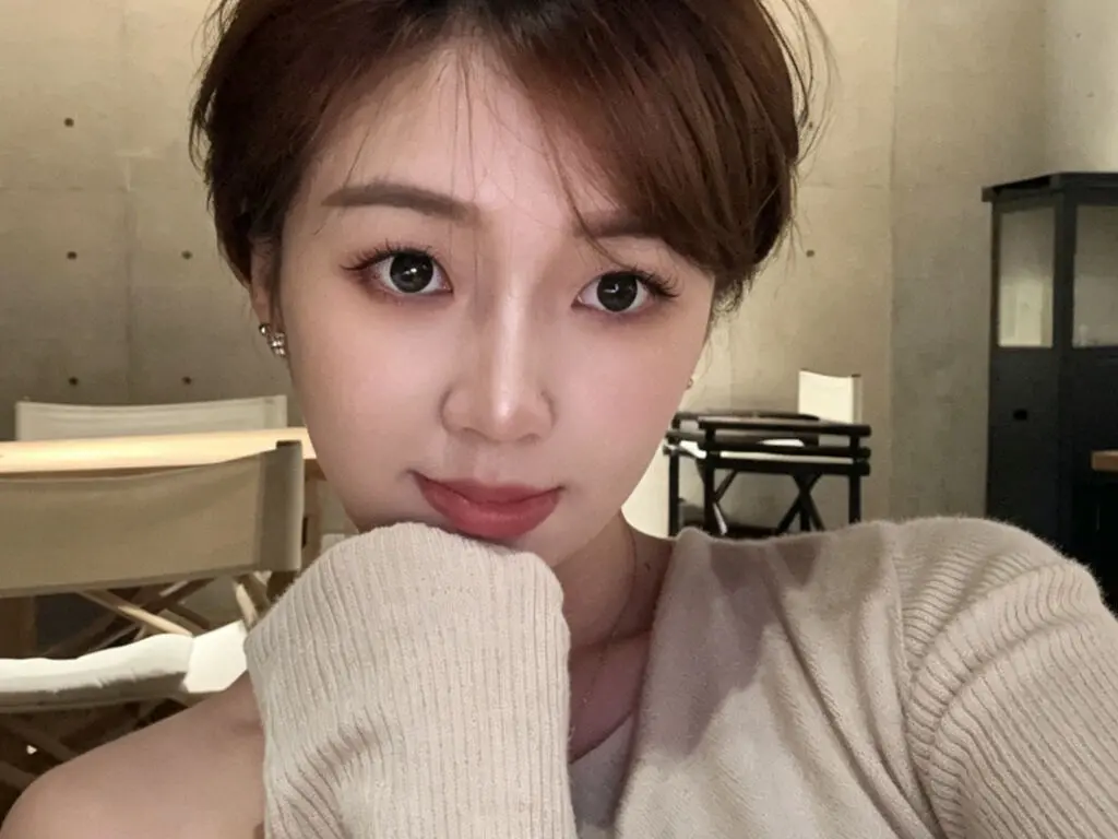 Young woman in a beige ribbed sweater smiling softly in a cozy cafe setting.