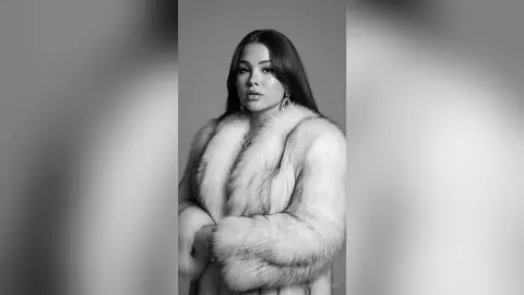 Elegant woman in a luxurious white faux fur coat posing against a minimalist studio background.