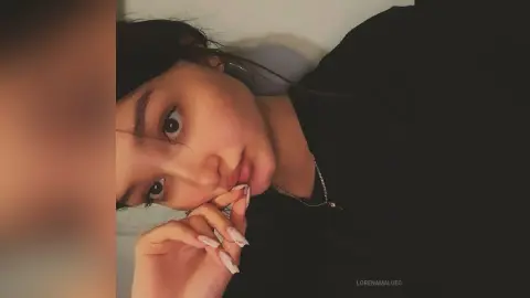 Young woman with dark hair wearing a black top posing for a moody close-up portrait indoors.