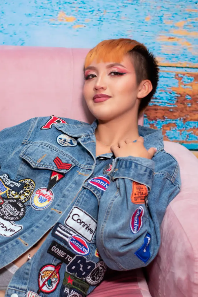 Smiling woman in a pink bikini top and jeans with body art posing on a staircase in warm lighting.