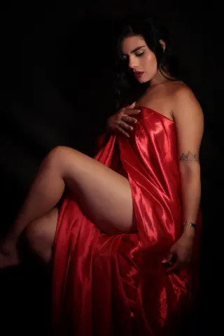 Elegant woman in a flowing red satin dress posing against a dark background for a moody, glamorous portrait.