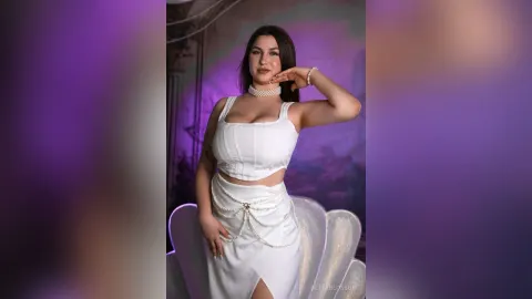 BettyBlossom — BettyBlossom poses in a white crop top and matching skirt with pearl accents against a purple background.