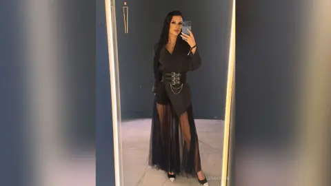 LeyaGrifin poses in a mirror wearing a black blazer, a belted waist, and a sheer black skirt.