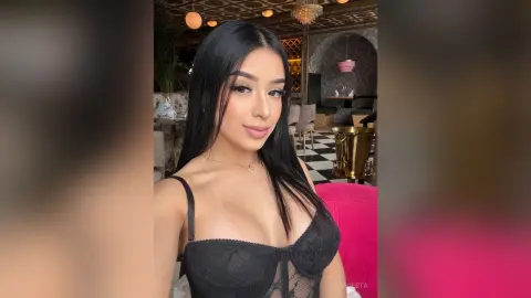 Beautiful woman in a black lace bodysuit posing in a stylish, modern restaurant setting.