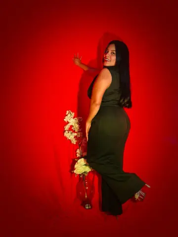 Smiling woman in a sleek black jumpsuit posing against a vibrant red background.