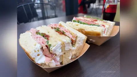 Freshly prepared ham and cream cheese sandwiches served in paper trays on a dark cafe table.