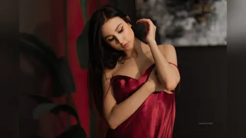 Elegant woman in a red satin slip dress posing thoughtfully in a moody, dark indoor setting.