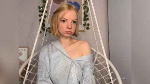 Blonde woman in a light blue checkered shirt sitting in a white hanging egg chair in a cozy room.