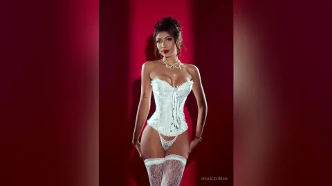 Glamorous woman in white lace corset and stockings posing against a bold red background.