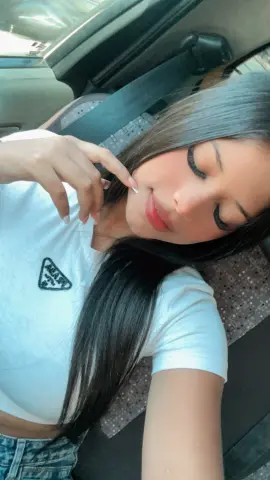 Young woman with long dark hair in a white t-shirt relaxing in a car seat with a peaceful expression.