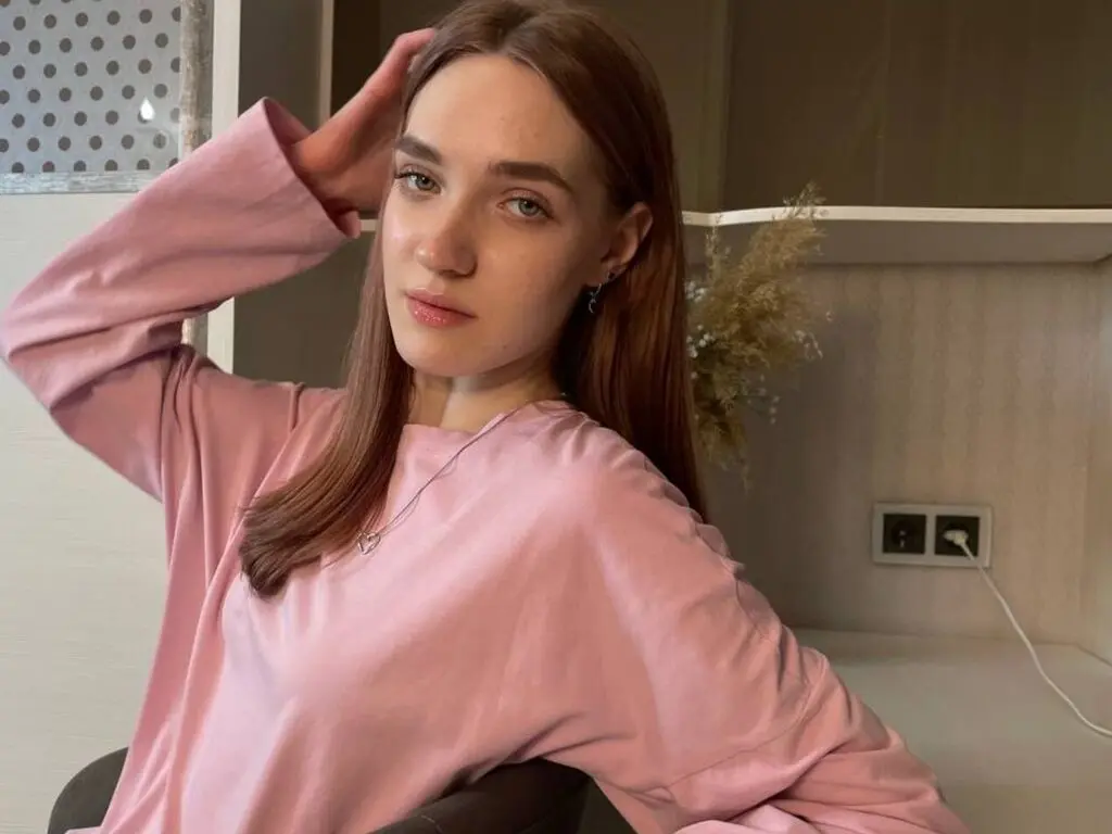 Young woman in a pink long-sleeve sweatshirt relaxing in a cozy indoor setting with a calm mood.