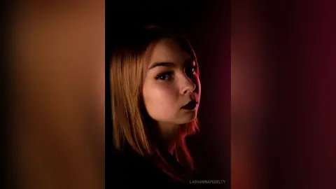 Moody portrait of a young woman with short brown hair in a dark, cinematic setting.
