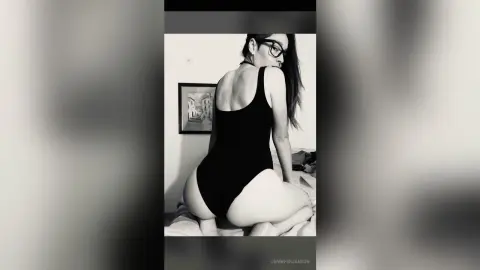 Black and white portrait of a woman in a black bodysuit posing in a minimalist indoor setting.